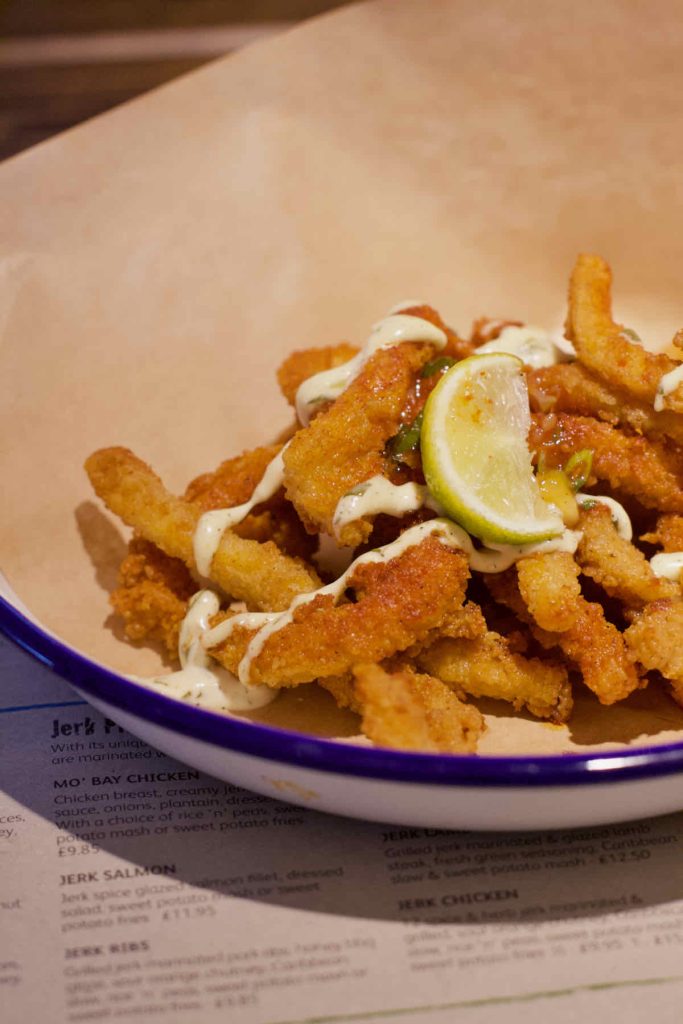 Deep fried breaded squid pieces with drizzle of mayo and wedge of lime on brown paper and in a white enamel dish with blue rim as served at Turtle Bay Caribbean style restaurant, Walthamstow branch East London.