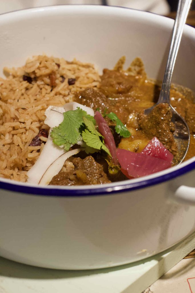 Goat curry with rice and peas served in white enamel dish with blue rim at Turtle Bay Caribbean style restaurant, Walthamstow branch East London