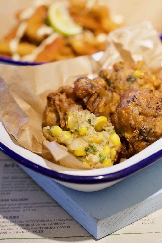 Deep fried sweetcorn fritters on brown paper in a white enamel dish with blue rim as served at Turtle Bay Caribbean style restaurant, Walthamstow branch East London.