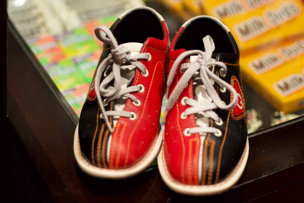 Red and black bowling shoes with white soles and white laces, as hired at All Star Lanes bowling alley, Westfield Stratford, East London. Some bars of American candy lie in soft focus behind.