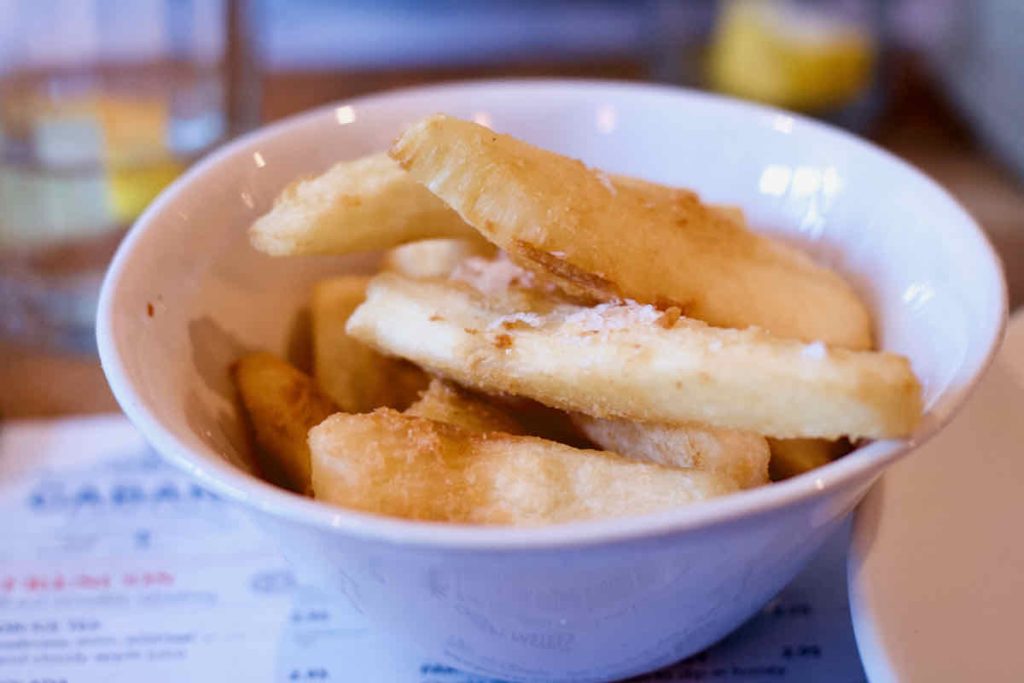 Thick golden Cassava chips in a white round dish, as served at Cabana Brazilian barbecue restaurant at Westfield Stratford branch East London. The menu, in soft focus is shown under the dish.