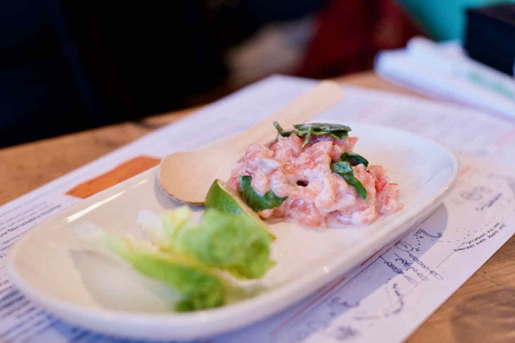 Salmon ceviche, chopped pink fish in white sauce with herb, lettuce and lime wedge garnish on oval white plate as served at Cabana Brazilian barbecue restaurant at Westfield Stratford branch East London.