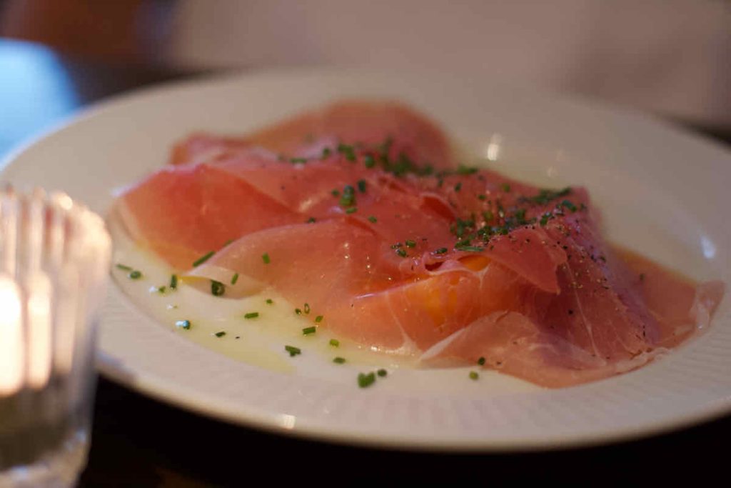 Cured ham served on top of melon with chopped herbs and olive oil on a white plate, as served at Cote Brasserie, Barbican Centre branch in the City of London