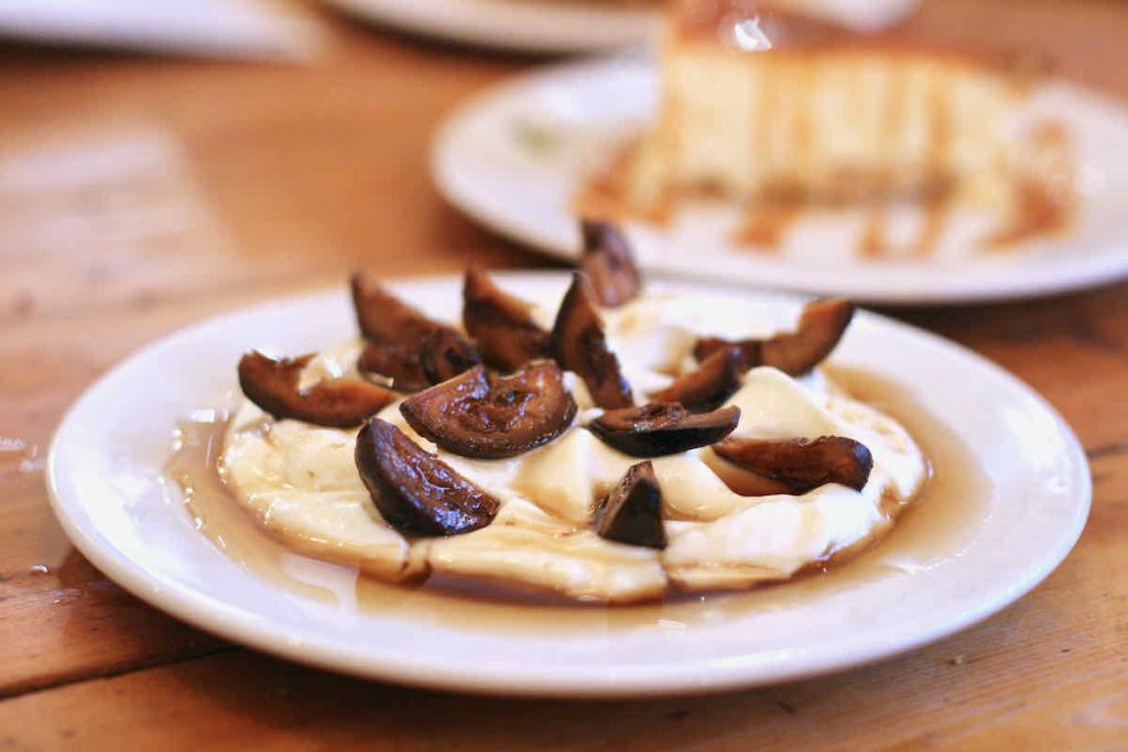 A white plate of Greek yogurt, dark brown walnut pieces and honey, as served at The Real Greek restaurant at Westfield Stratford, East London.